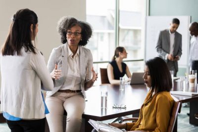 Mature African American businesswoman gestures during a planning session with female colleagues.